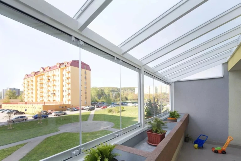 Nowoczesne bezramowe przeszklenie balkonu z widokiem na osiedle i zieleń