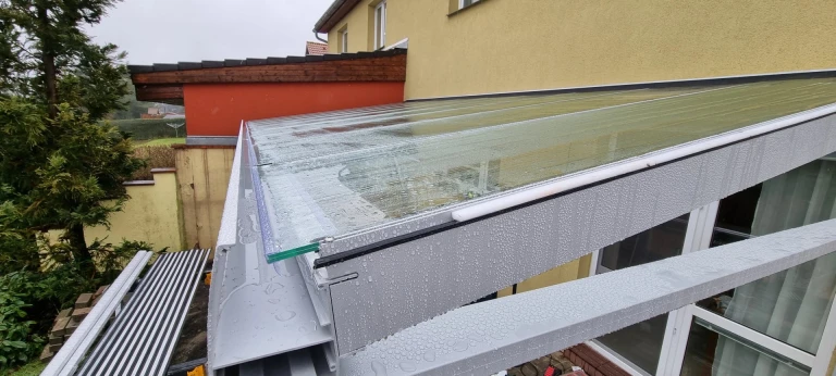 Szczegółowe ujęcie zadaszenia aluminiowej pergoli ze szklanym wypełnieniem pokrytym kroplami deszczu.