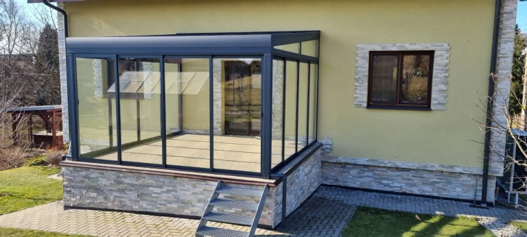 Zaszklona pergola aluminiowa ROBUST dobudowana do domu jednorodzinnego, wyposażona w schodki