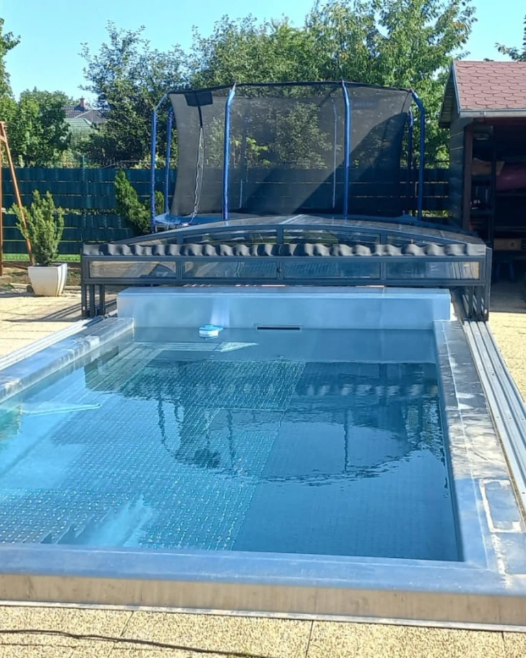 Nowoczesny basen z cofniętym, niskim zadaszeniem w ogrodzie z trampoliną.