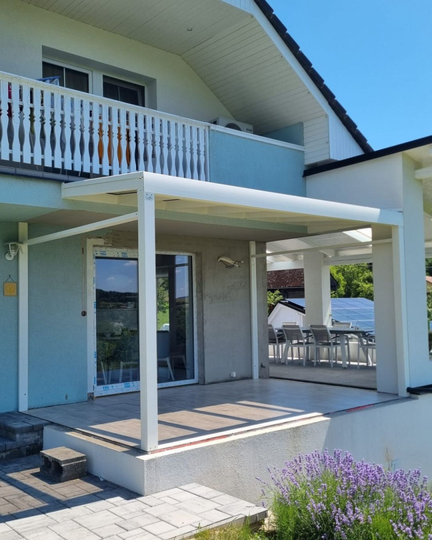 Nowoczesna, biała pergola z aluminium przylegająca do domu jednorodzinnego z tarasem i lawendą na pierwszym planie