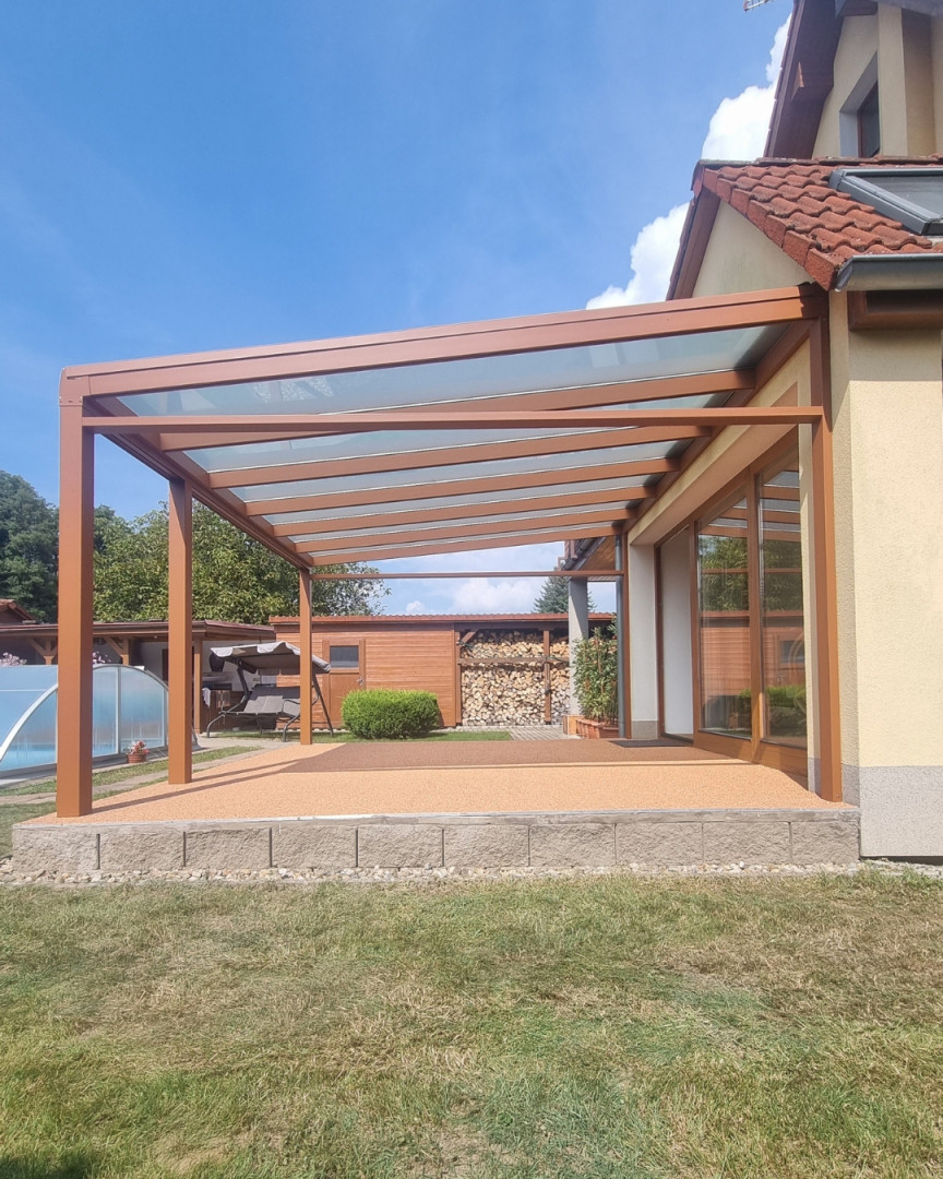 Brązowa pergola aluminiowa ze szklanym dachem, dobudowana do domu jednorodzinnego