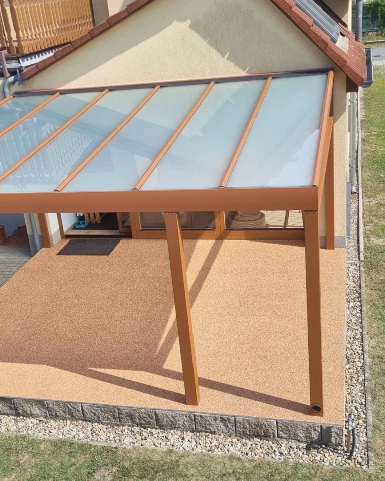Nowoczesna pergola aluminiowa z mlecznym przeszkleniem i brązową konstrukcją, zamontowana przy ścianie domu