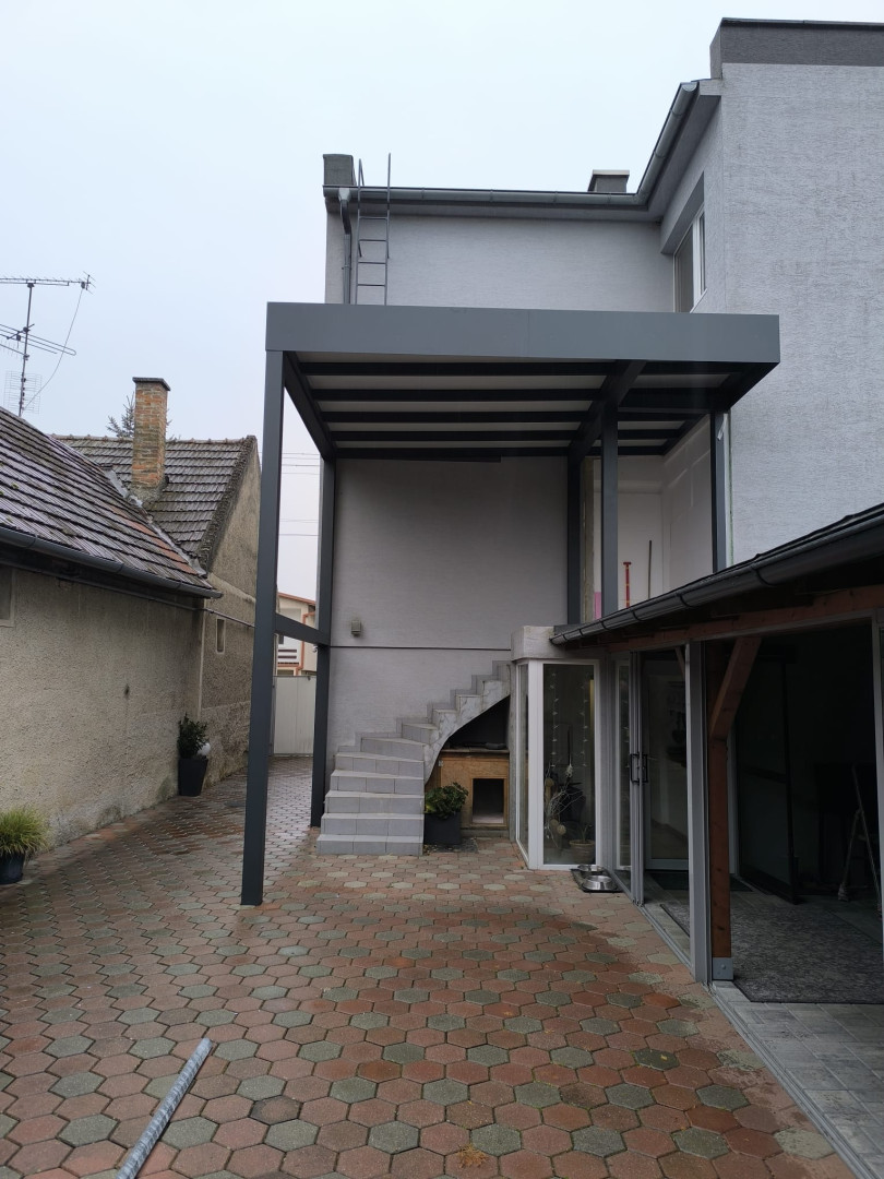 Nowoczesna, szara pergola z aluminium, wykonana na zamówienie i zamontowana na tarasie domu jednorodzinnego nad zewnętrznymi schodami.