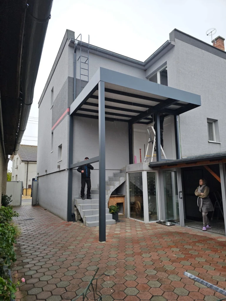 Nowoczesna, szara pergola z aluminium zamontowana nad klatką schodową domu jednorodzinnego