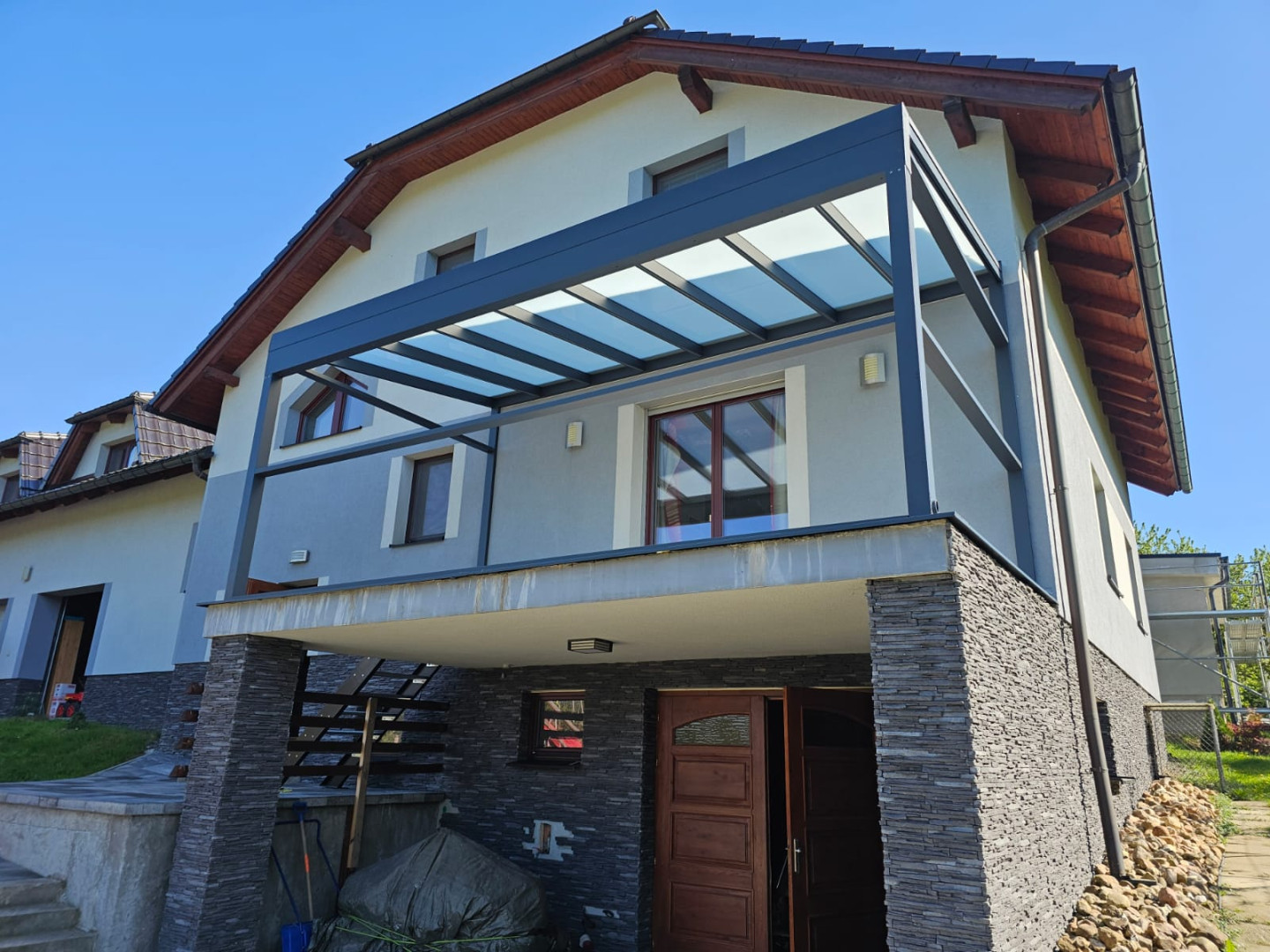 Nowoczesna pergola aluminiowa ze szklanym dachem zamontowana na balkonie domu jednorodzinnego