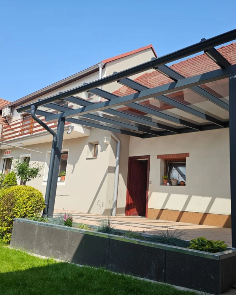 Nowoczesna antracytowa pergola aluminiowa ze szklanym dachem, dobudowana do domu jednorodzinnego
