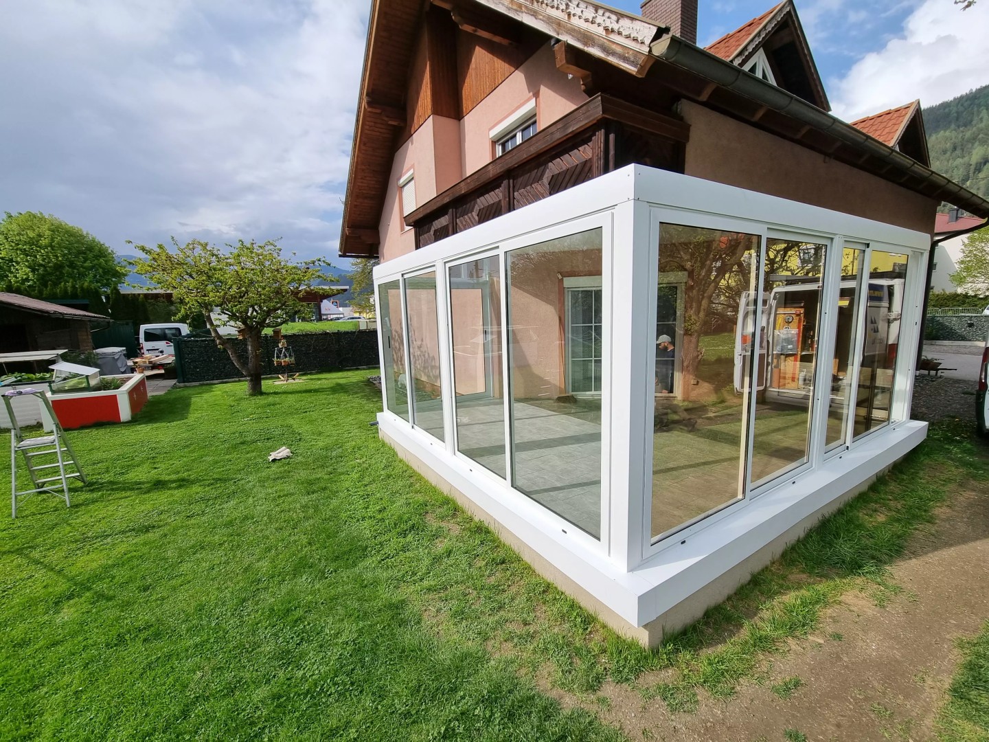 Nowoczesna, biała, przeszklona pergola z aluminium przy domu jednorodzinnym w ogrodzie.