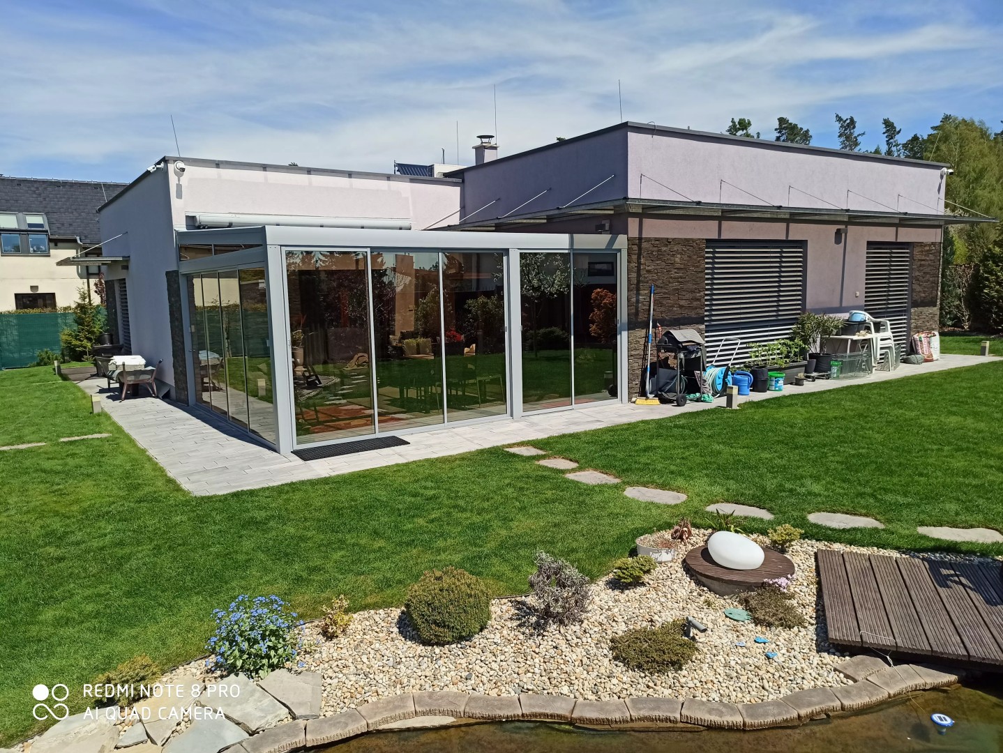 Nowoczesna aluminiowa pergola z przeszkleniem przy domu jednorodzinnym w ogrodzie