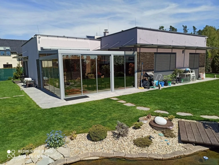 Nowoczesna aluminiowa pergola z przeszkleniem przy domu jednorodzinnym w ogrodzie