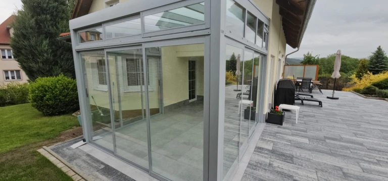 Nowoczesny, przeszklony ogród zimowy z aluminiową konstrukcją, zbudowany na przestronnym tarasie domu jednorodzinnego.