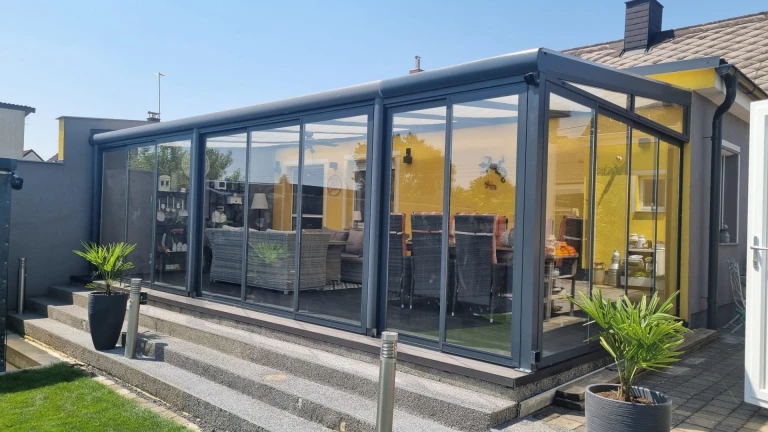 Nowoczesny, przeszklony ogród zimowy z aluminium w kolorze antracytowym z przesuwnymi drzwiami na tarasie domu.