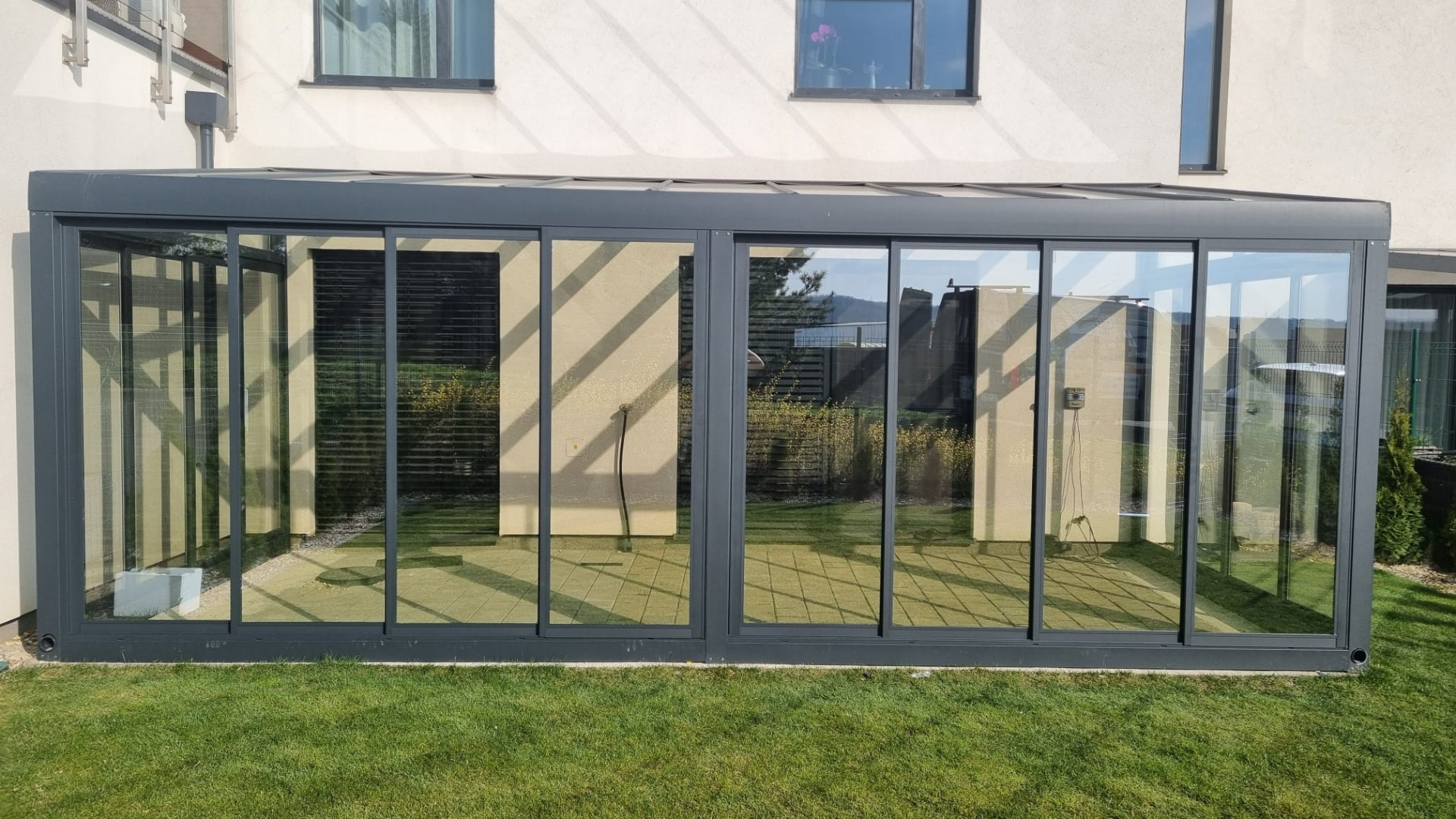 Nowoczesny, przeszklony ogród zimowy z aluminiową konstrukcją przy domu jednorodzinnym, z widokiem na trawnik.