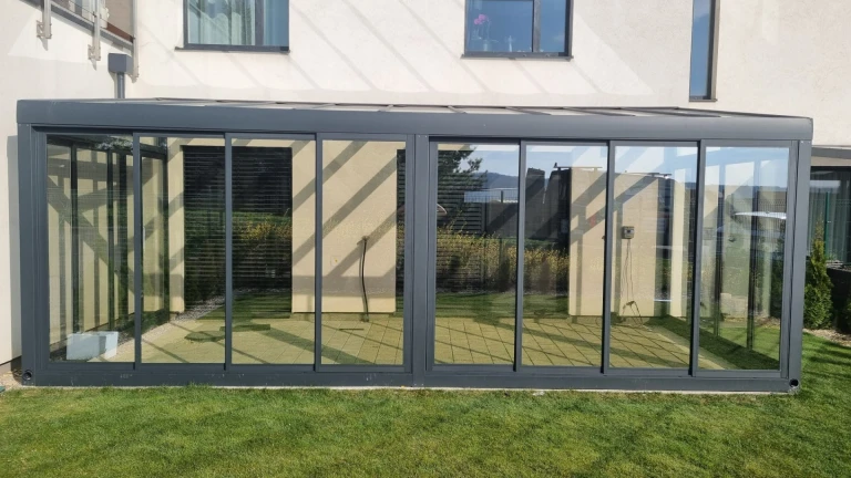 Nowoczesny, przeszklony ogród zimowy z aluminiową konstrukcją przy domu jednorodzinnym, z widokiem na trawnik.