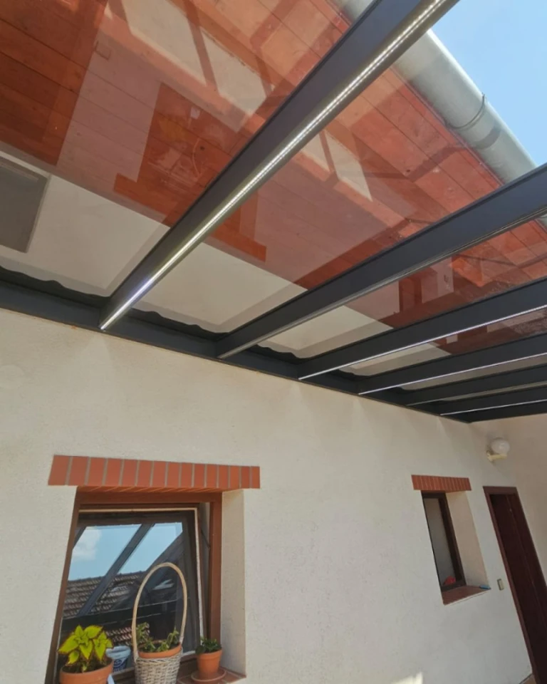 Szczegółowe ujęcie zadaszenia aluminiowej pergoli z wbudowanym oświetleniem LED, przymocowanej do elewacji domu.