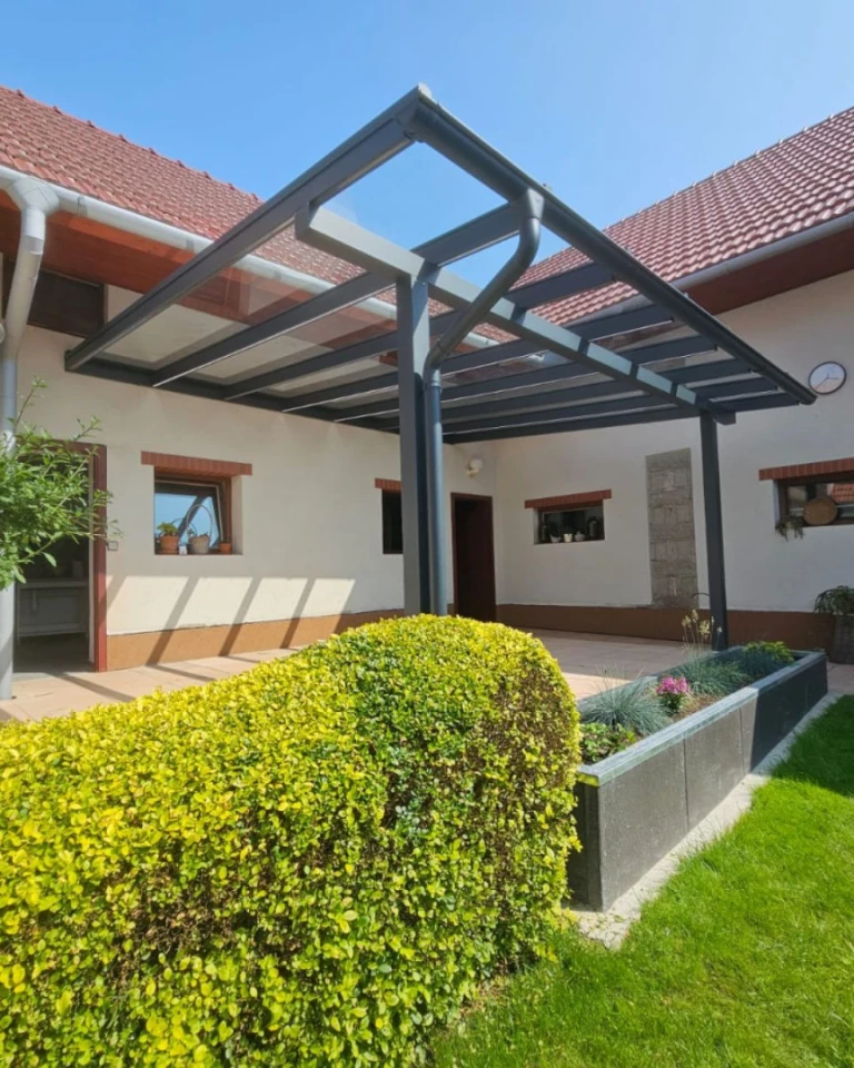 Nowoczesna pergola aluminiowa ze szklanym dachem, dobudowana do domu jednorodzinnego z zadbanym ogrodem.