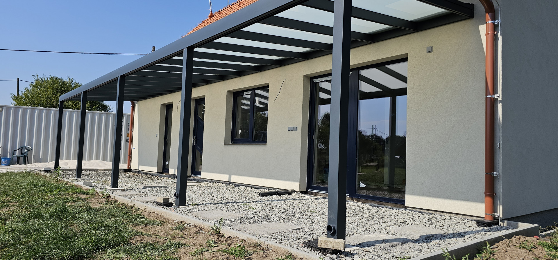 Nowoczesna pergola aluminiowa ze szklanym dachem, przymocowana do ściany domu jednorodzinnego