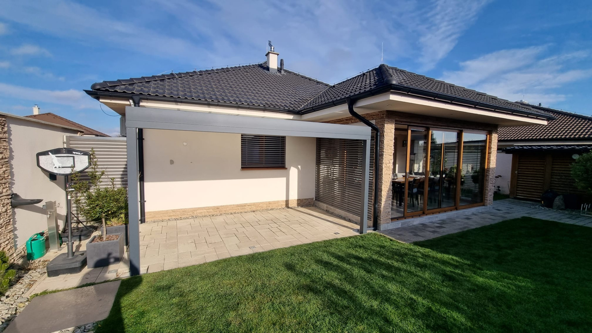 Nowoczesna, szara pergola z aluminium przy bungalowie, na wybrukowanym tarasie przy ogrodzie