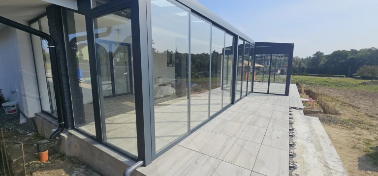 Nowoczesny, przeszklony ogród zimowy z antracytową konstrukcją aluminiową i wyłożonym płytkami tarasem.