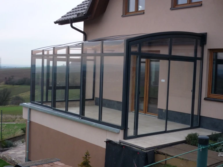 Nowoczesna przesuwna oranżeria z antracytową konstrukcją aluminiową i przeszkleniem na tarasie domu jednorodzinnego.