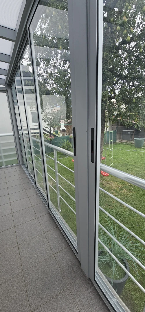 Szczegółowe ujęcie przesuwnych szklanych drzwi i balustrady ogrodu zimowego z widokiem na zielony ogród.