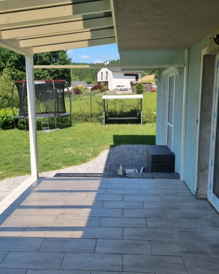 Widok spod budowanej aluminiowej pergoli na ogród z trampoliną i huśtawką