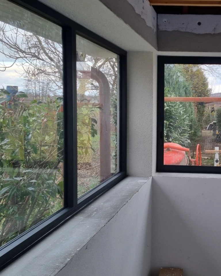 Szczegółowe ujęcie narożnego przeszklenia tarasu z ciemnymi ramami aluminiowymi i widokiem na ogród.