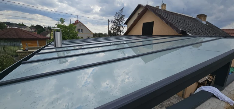 Widok z góry na przeszklony dach nowoczesnego ogrodu zimowego z ciemną konstrukcją przy domu jednorodzinnym