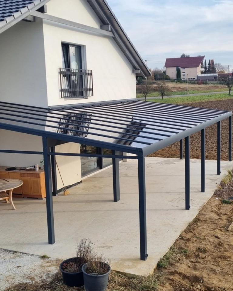 Nowoczesna pergola aluminiowa ze szklanym dachem i ciemną konstrukcją przy domu jednorodzinnym