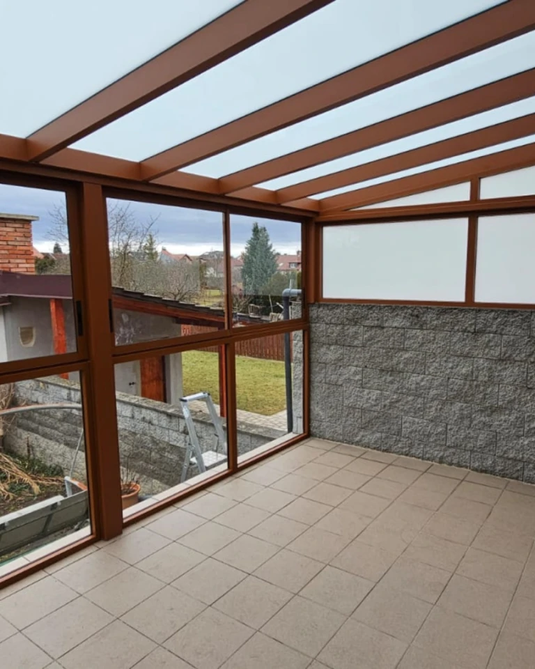 Zaszklona pergola aluminiowa z brązową konstrukcją i widokiem na ogród