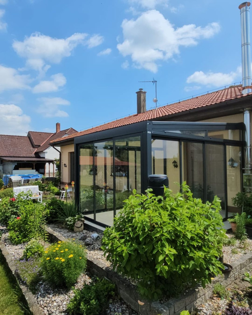 Nowoczesny, przeszklony ogród zimowy z antracytową konstrukcją przy domu jednorodzinnym z zadbanym ogrodem